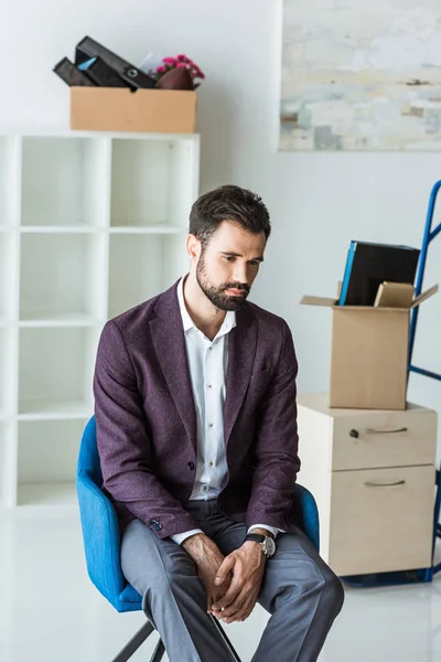 Deprimido despedido hombre de negocios sentado en la silla en la oficina vacía - foto de stock