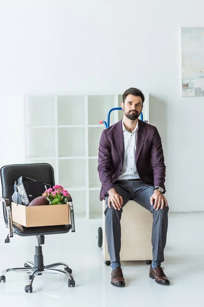 Entlassener junger Geschäftsmann mit Kiste voller persönlicher Sachen sitzt auf Einkaufswagen — Stockfoto