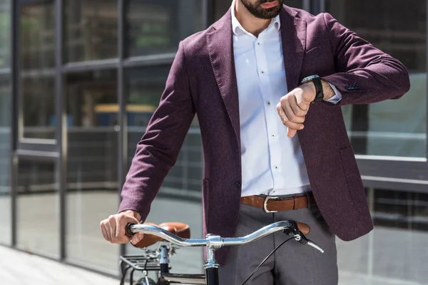 Обрезанный снимок мужчины в стильном костюме с винтажным велосипедом, смотрящим на часы — стоковое фото