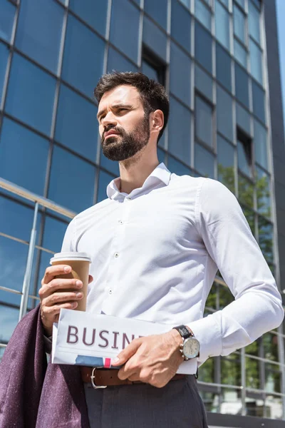 Vista inferior de belo jovem empresário com café para ir e jornais ao ar livre — Fotografia de Stock