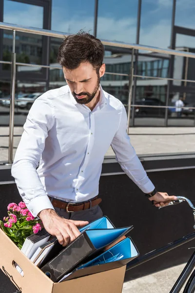Молодий менеджер кладе коробку особистих речей на велосипедний багажник — стокове фото