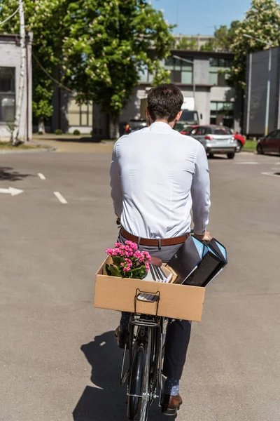 Vista trasera del gerente montando en bicicleta con caja de cosas personales en el maletero - foto de stock