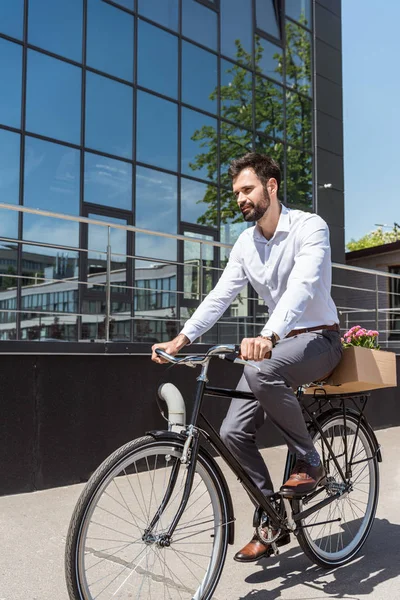 Jovem gerente feliz andando de bicicleta com caixa no tronco — Fotografia de Stock