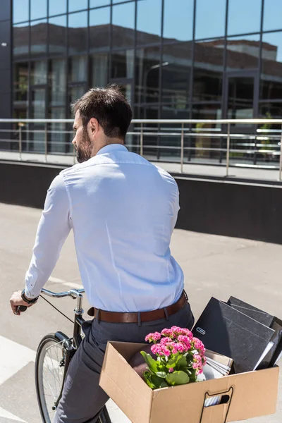 Вид сзади на молодого менеджера, катающегося на велосипеде с коробкой на багажнике — стоковое фото