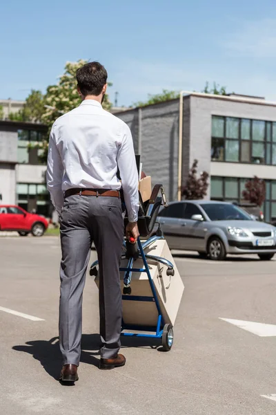 Rear view of fired young manager with boxes on trolley cart at parking — Stock Photo