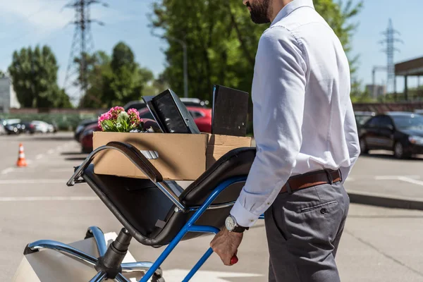 Schuss auf gefeuerten jungen Manager mit Kisten auf Einkaufswagen auf Parkplatz — Stockfoto