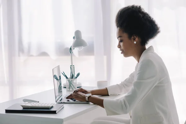 Vue latérale d'une femme d'affaires afro-américaine attrayante utilisant un ordinateur portable au bureau — Photo de stock