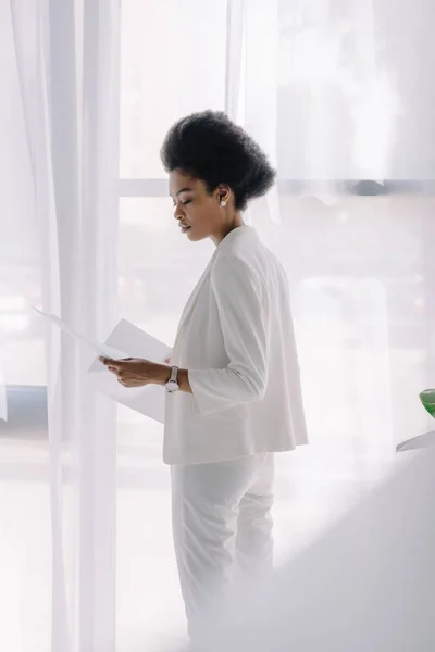 Vue latérale d'une femme d'affaires afro-américaine attrayante lisant des documents au bureau — Photo de stock