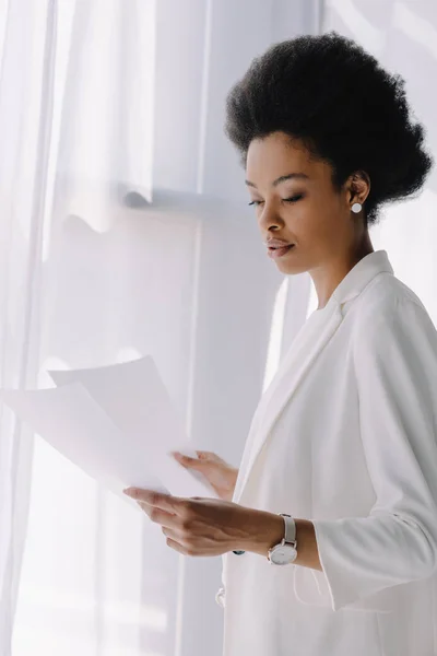 Atractiva mujer de negocios afroamericana leyendo documentos en la oficina - foto de stock