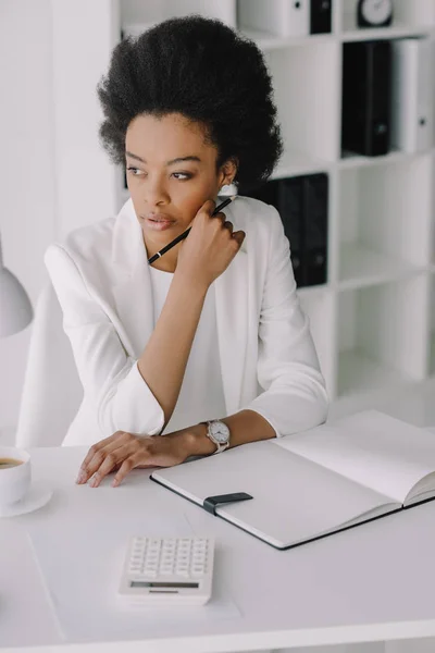 Attraktive nachdenkliche afrikanisch-amerikanische Geschäftsfrau am Tisch sitzend und im Büro wegschauend — Stockfoto