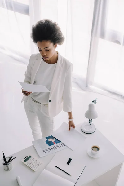 Vista de ángulo alto del documento atractivo de la lectura de la mujer de negocios afroamericana en oficina - foto de stock