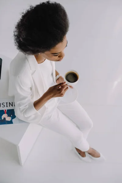 Hochwinkelaufnahme der schönen afrikanisch-amerikanischen Geschäftsfrau, die mit einer Tasse Kaffee im Büro auf dem Tisch sitzt — Stockfoto