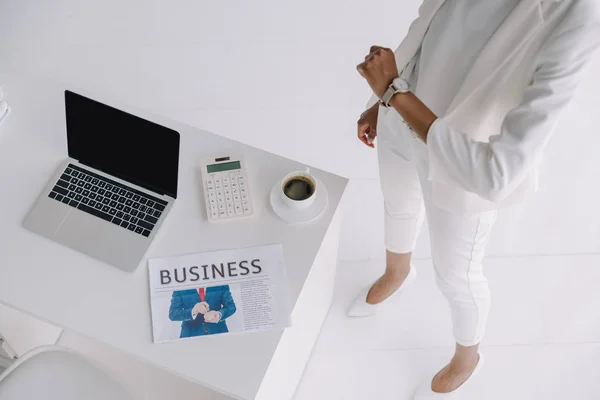 Imagen recortada de la mujer de negocios afroamericana de pie cerca de la mesa de trabajo en la oficina y comprobar el tiempo - foto de stock