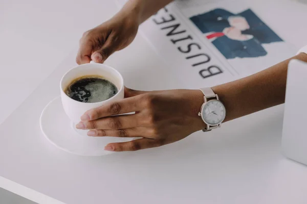 Imagem recortada de empresária afro-americana segurando xícara de café à mesa com jornal no escritório — Fotografia de Stock