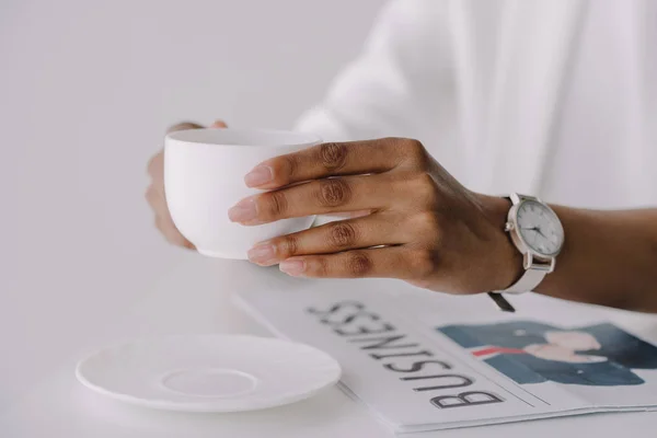 Immagine ritagliata di donna d'affari afro-americana in possesso di una tazza di caffè a tavola in ufficio — Foto stock