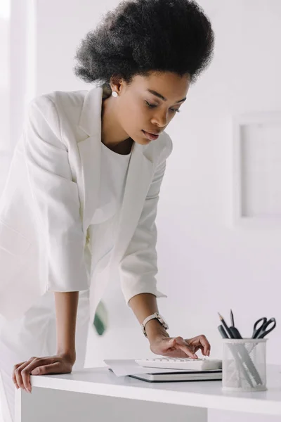 Atractiva mujer de negocios afroamericana utilizando la calculadora en la oficina - foto de stock