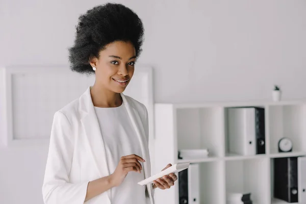 Atractiva mujer de negocios afroamericana sosteniendo calculadora en la oficina - foto de stock