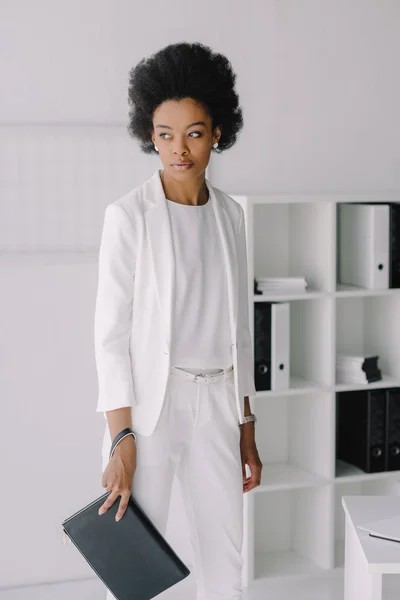 Séduisante femme d'affaires afro-américaine debout avec un petit sac au bureau — Photo de stock