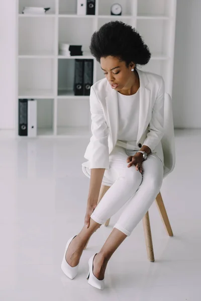 Atractiva mujer de negocios afroamericana tocando el tobillo en la oficina - foto de stock
