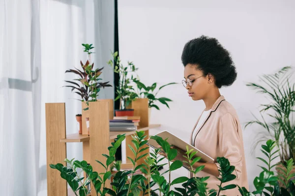 Visão lateral da atraente mulher de negócios afro-americana segurando notebook no escritório — Fotografia de Stock