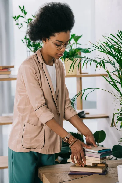 Attractive african american businesswoman putting books on table in office — Stock Photo