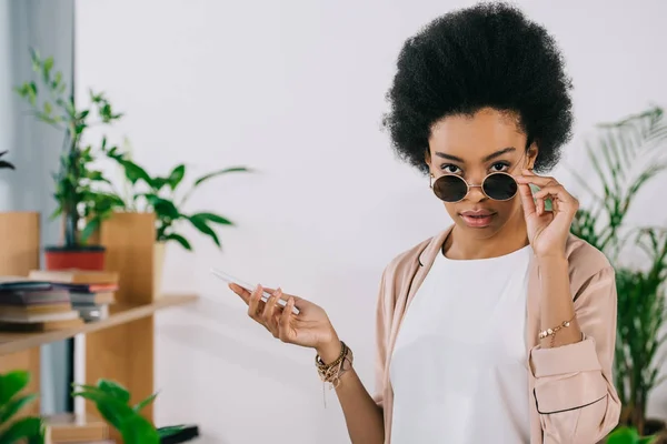 Attractive african american businesswoman looking above sunglasses in office — Stock Photo