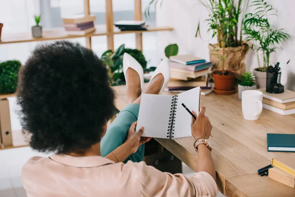 Back view of african american businesswoman holding notebook and pencil in office — Stock Photo