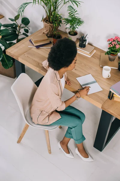 Vista ad alto angolo della donna d'affari afro-americana che legge appunti nel quaderno in ufficio — Foto stock