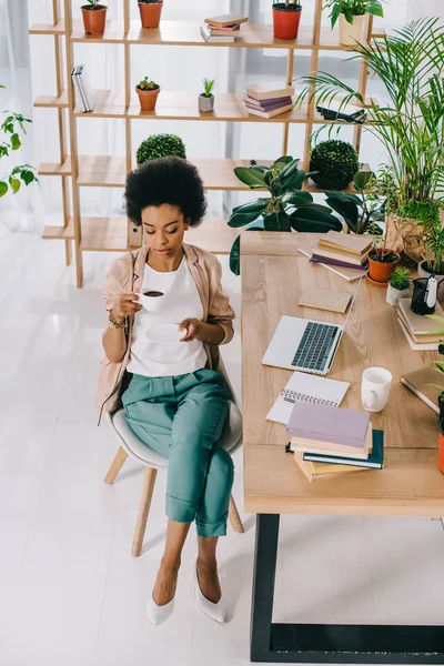 Vista ad alto angolo di attraente donna d'affari africana americana che beve caffè durante la pausa caffè in ufficio — Foto stock