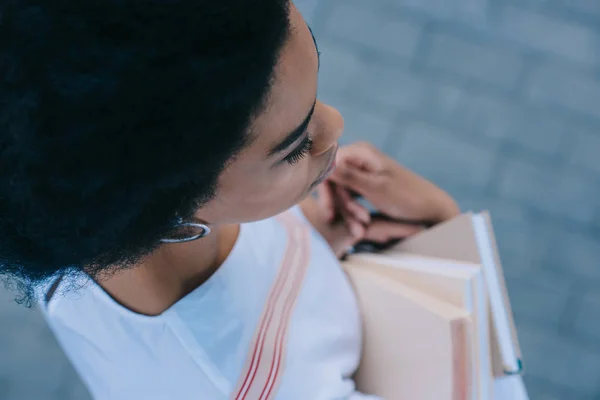 Vista de ángulo alto de la atractiva mujer de negocios afroamericana de pie con libros en la calle - foto de stock