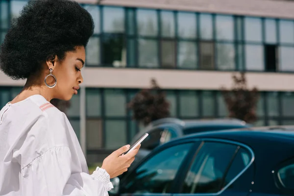 Vue latérale de la femme d'affaires afro-américaine attrayante en utilisant un smartphone sur le parking — Photo de stock
