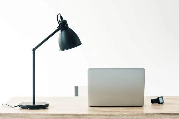 Ноутбук, умные часы и лампа на деревянном столе в офисе — стоковое фото