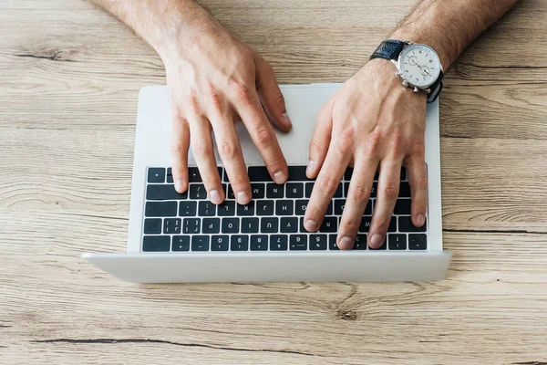 Close-up partial view of person typing on laptop at wooden table — Stock Photo