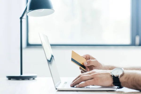 Cropped shot of person holding credit card and using laptop at workplace — Stock Photo