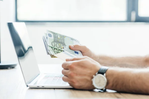 Partial view of person holding credit card and euro banknotes at workplace — Stock Photo