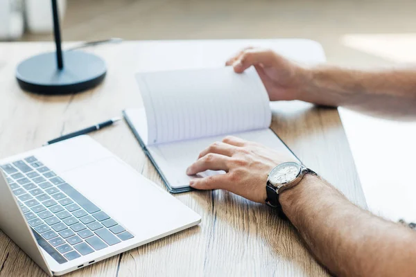 Primer plano vista parcial de la persona que sostiene un cuaderno en blanco en el lugar de trabajo - foto de stock