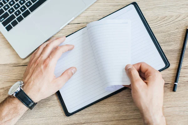 Vue de dessus partielle de la personne tenant un cahier vierge sur le lieu de travail — Photo de stock