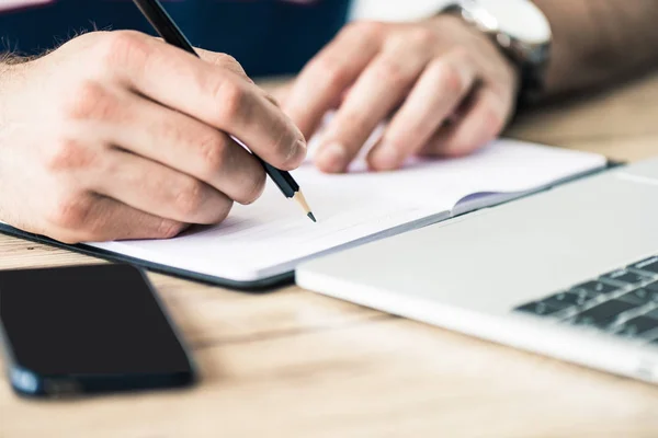 Cropped shot of person writing in notebook at wooden table — Stock Photo