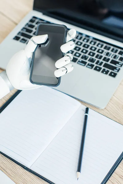 Close-up view of hand of robot holding smartphone with blank screen at workplace — Stock Photo