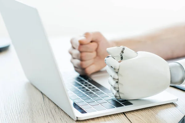 Close-up view of human and robot fists on laptop at wooden table — Stock Photo