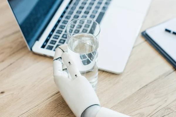 Close-up view of hand of robot holding glass of water at wooden table — Stock Photo