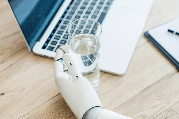 Vista de cerca de la mano del robot sosteniendo el vaso de agua en la mesa de madera - foto de stock