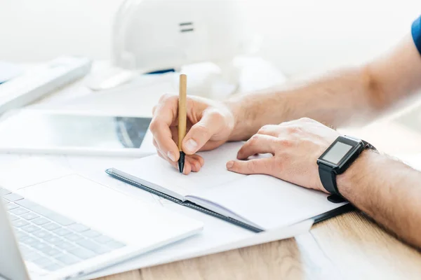 Partial view of person wearing smartwatch and taking notes at workplace — Stock Photo