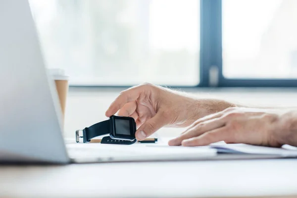 Colpo ritagliato di persona che tiene smartwatch e utilizzando il computer portatile sul posto di lavoro — Foto stock