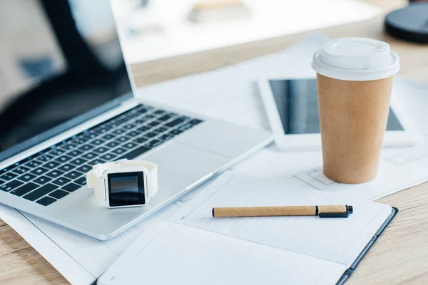 Vista close-up de smartwatch, laptop, notebook e xícara de café descartável no local de trabalho — Fotografia de Stock