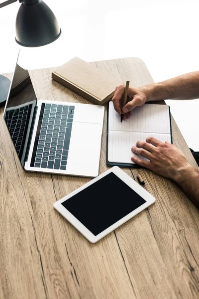 Visão de alto ângulo da pessoa tomando notas e trabalhando com laptop e tablet digital na mesa de madeira — Fotografia de Stock