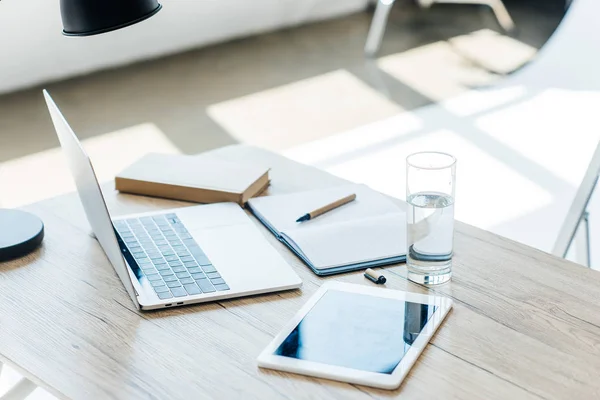 Laptop, digitales Tablet, Wasserglas, Buch und Notizbuch am Arbeitsplatz — Stockfoto