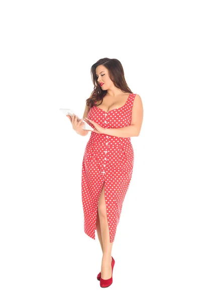 Красива жінка плюс розмір в червоній точковій сукні з використанням планшета ізольована на білому — стокове фото