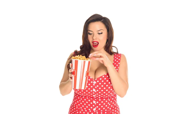 Shocked plus size woman in red dress eating popcorn isolated on white — Stock Photo