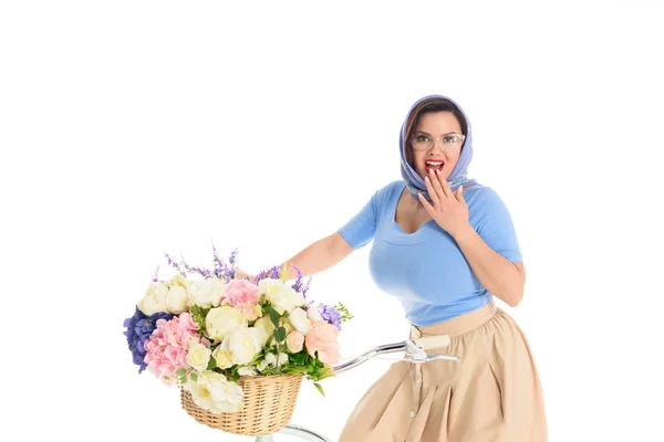 Удивлена молодая женщина сидит на велосипеде с корзиной цветов и улыбаясь на камеру изолированы на белом — стоковое фото